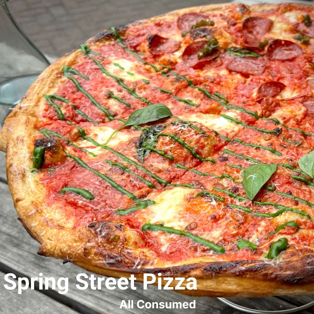 A close-up of a delicious New York style pizza topped with tomato sauce, mozzarella cheese, sliced pepperoni, and fresh basil, served at Spring Street Pizza.